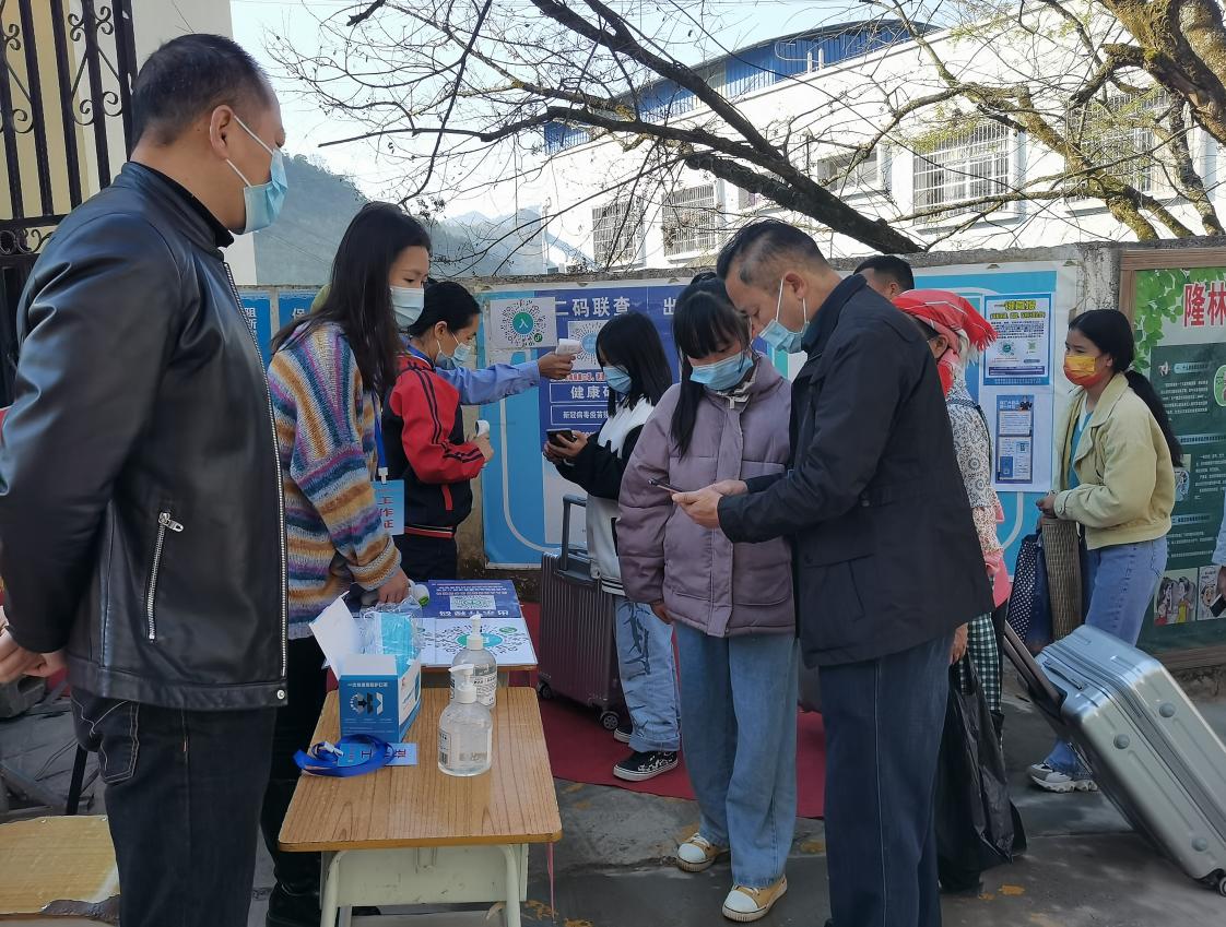 图为猪场乡乡长(左一)和猪场乡小学校长(右一)在校门现场指导返校学生扫验各校健康码和行程码